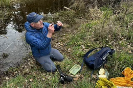 Brian Starzomski takes a photo of a vile as he sits beside a small pond.