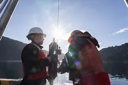 Two people wearing protective gear hold equipment on a boat.