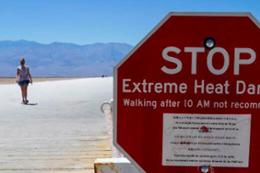 A person walks on the road with a stop extreme heat danger sign in the forefront.