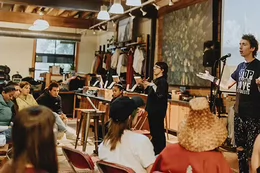 Two people stand and speak to a group seated facing them. 