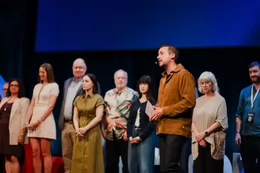 A group of people stand on a stage at a TEDx event. One person has a microphone.