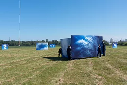 People dressed in back hold up canvases of clouds in a field.