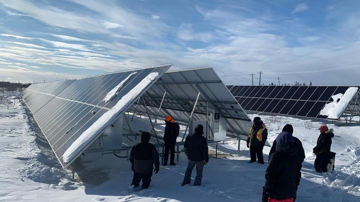 Participants of the Community Energy Systems Course in Old Crow, Yukon, March 2023. Participants stand next to rows of solar panels surrounded by snow.