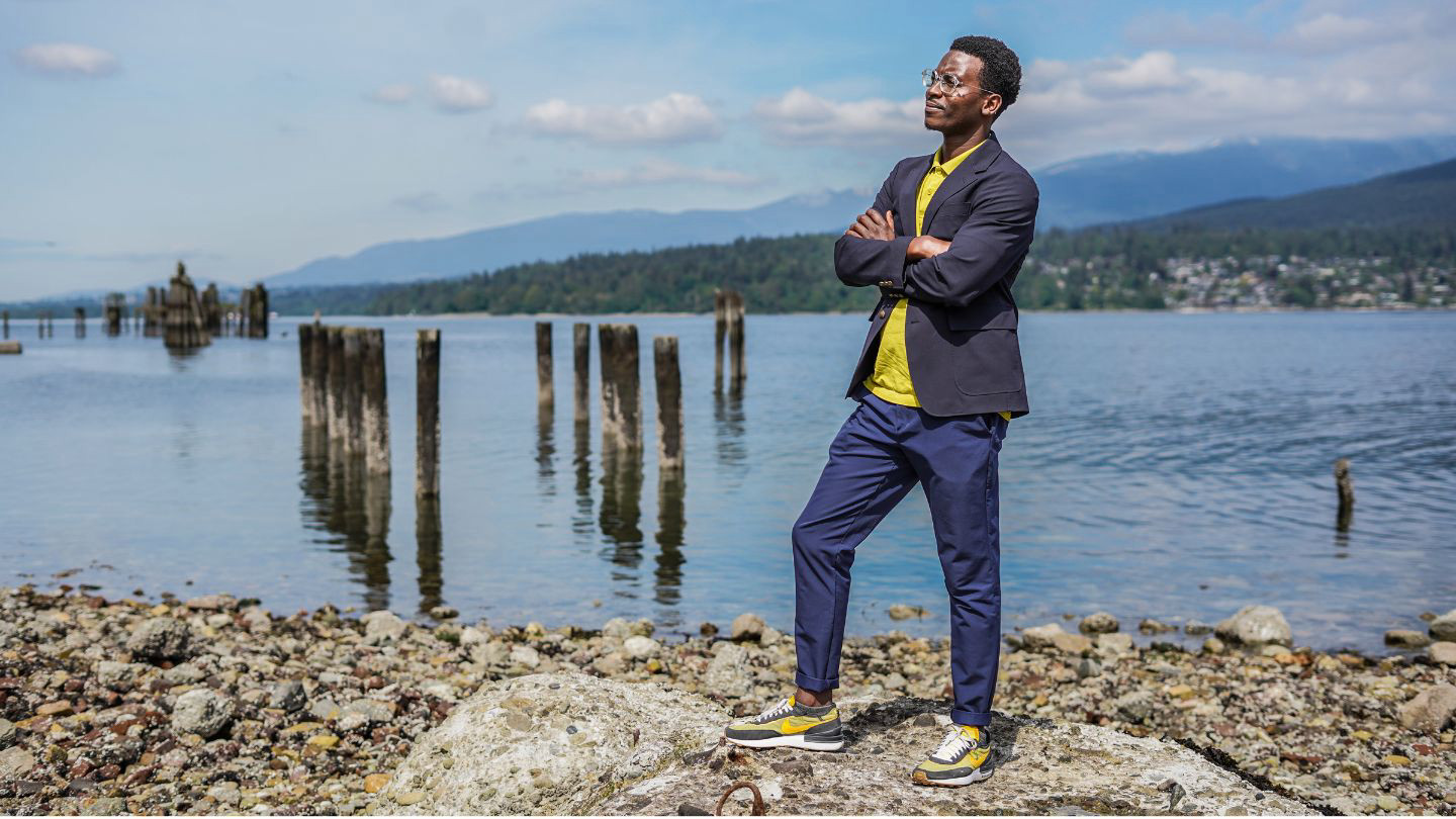 A person wearing a suit and brightly coloured shoes posing by the ocean