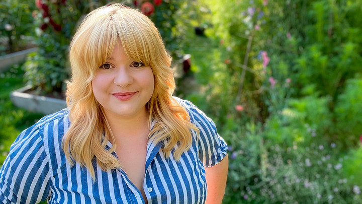 Woman student in striped blue shirt with garden behind her