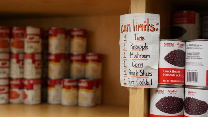 Wood shelves with cans of soup and beans on them. A sign reads can limits: 1 tuna, 1 pineapple, 1 mushroom, 1corn, 1 peach slices, 1 fruit cocktail