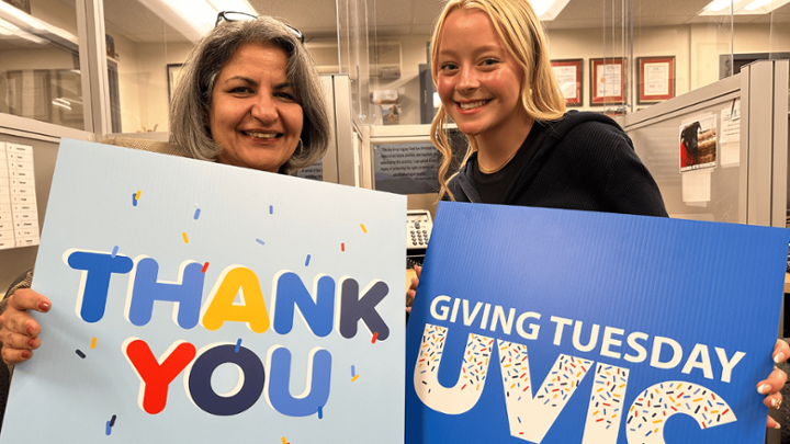 Anita Bhappu smiles with a student caller. They are holding signs saying "thank you" and "Giving Tuesday UVic"