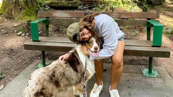 A female student sitting on a bench in the forest hugging a fluffy brown and white dog