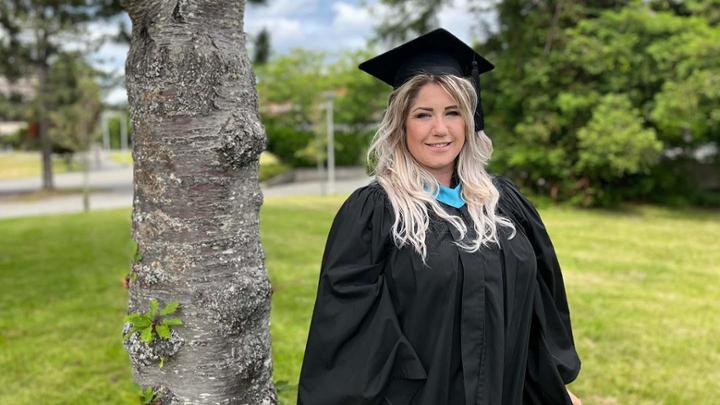 Student in cap and gown outside on UVic campus