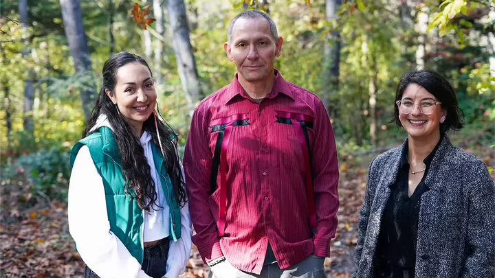 Three students in a forest setting looking at camera