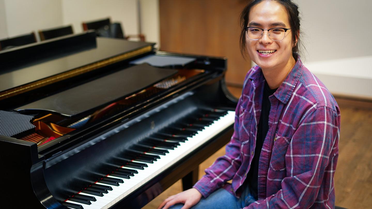 Lucas Hung sits at the piano smiling at the camera