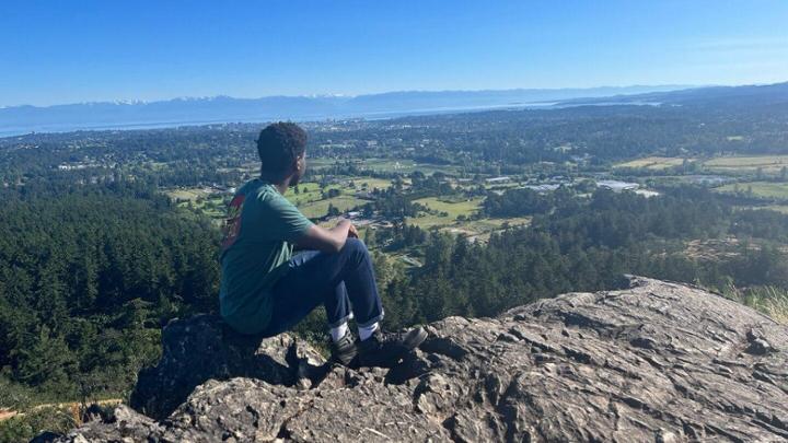 Student sitting on rocky hilltop looking out on view of Vancouver Island and ocean