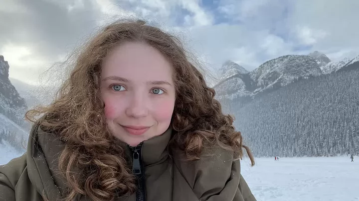A person in a parka close to camera with snow scene and mountains in background