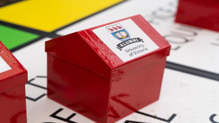 A red monopoly board piece on a board with a UVic Alumni logo sticker on the roof