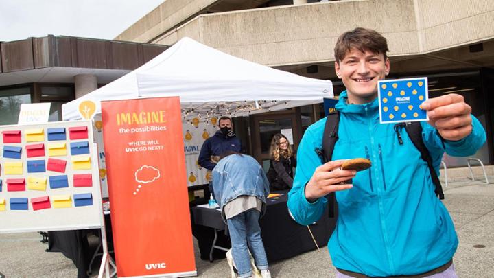Student in blue jacket smiling while standing in front of "Imagine UVic" booth.