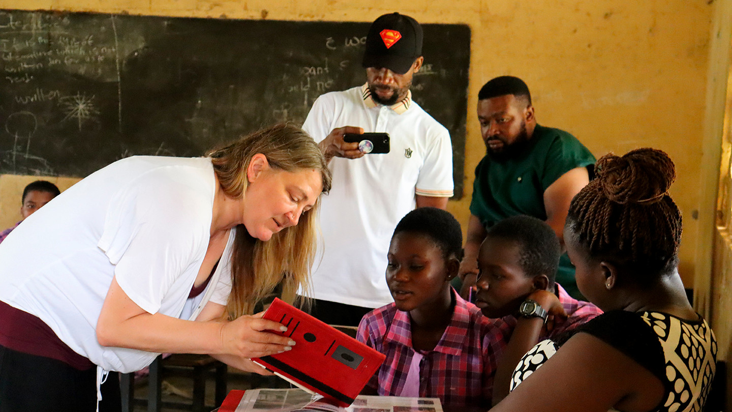 A woman and three middle school children view a handheld device