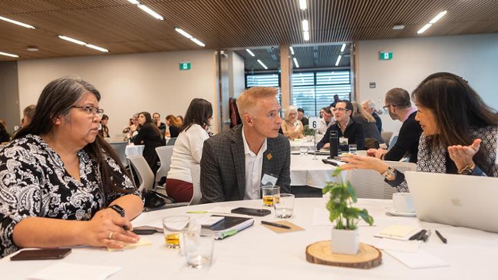 Three particpants sit around a table discussing a question topic