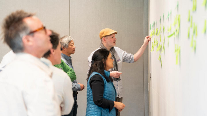 Researchers stand in front of a wall, categorizing coloured sticky notes with ideas on them