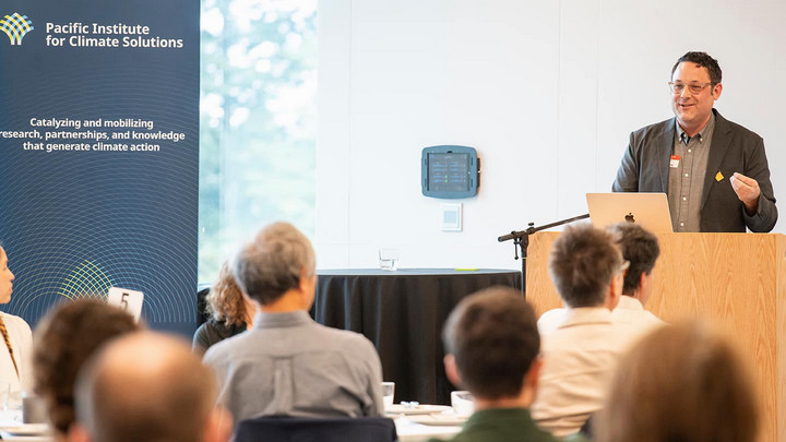 Ian Mauro stands at a podium addressing the room of researchers