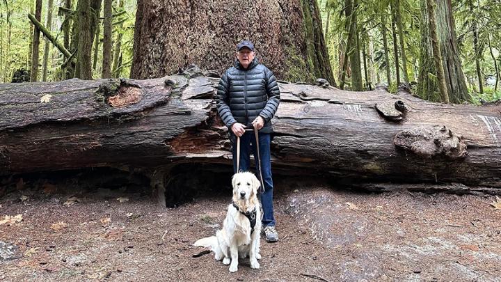 Fulbright Scholar Brent Steel stands in a forest with his dog in front 