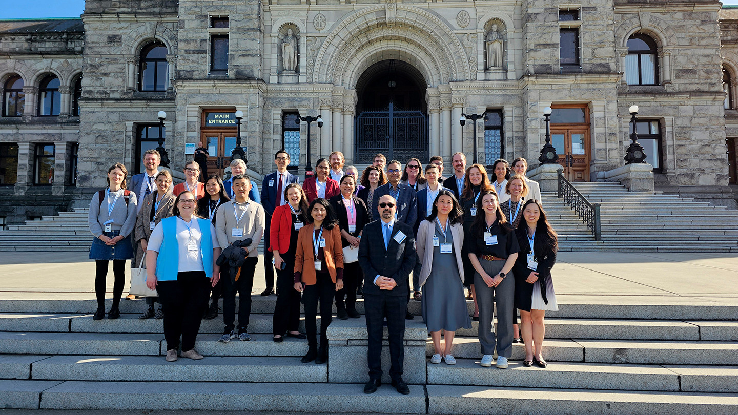 A large group of researchers stand outside the Legislative Assembly of BC