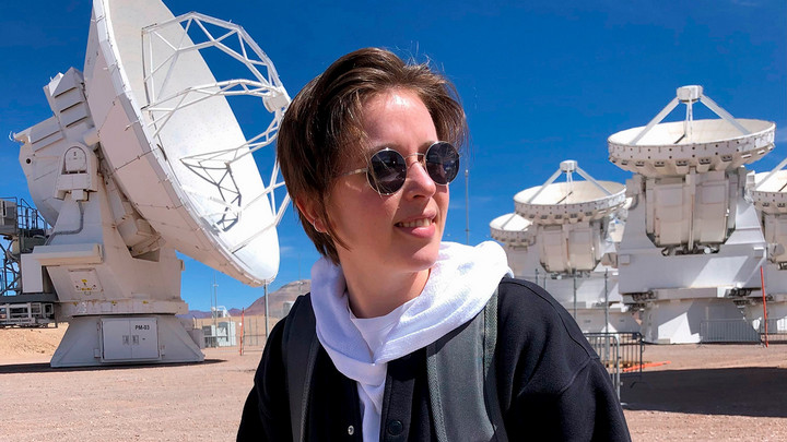 Jess Speedie stands in front of telescopes at ALMA