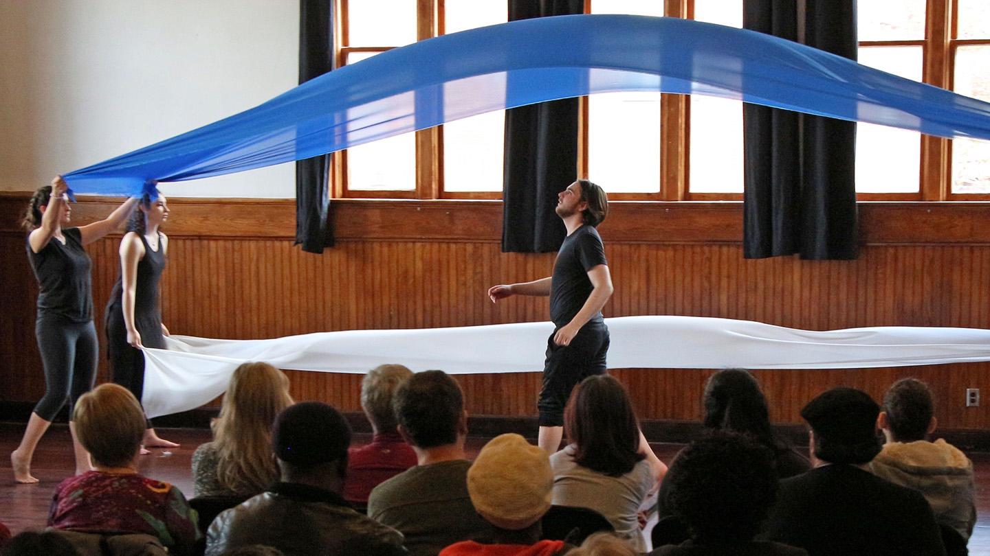 a group of performers wave blue silk fabric across the stage as part of a performance