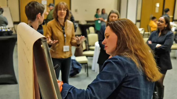 Tamara Krawchenko writes on a white board in a busy conference room