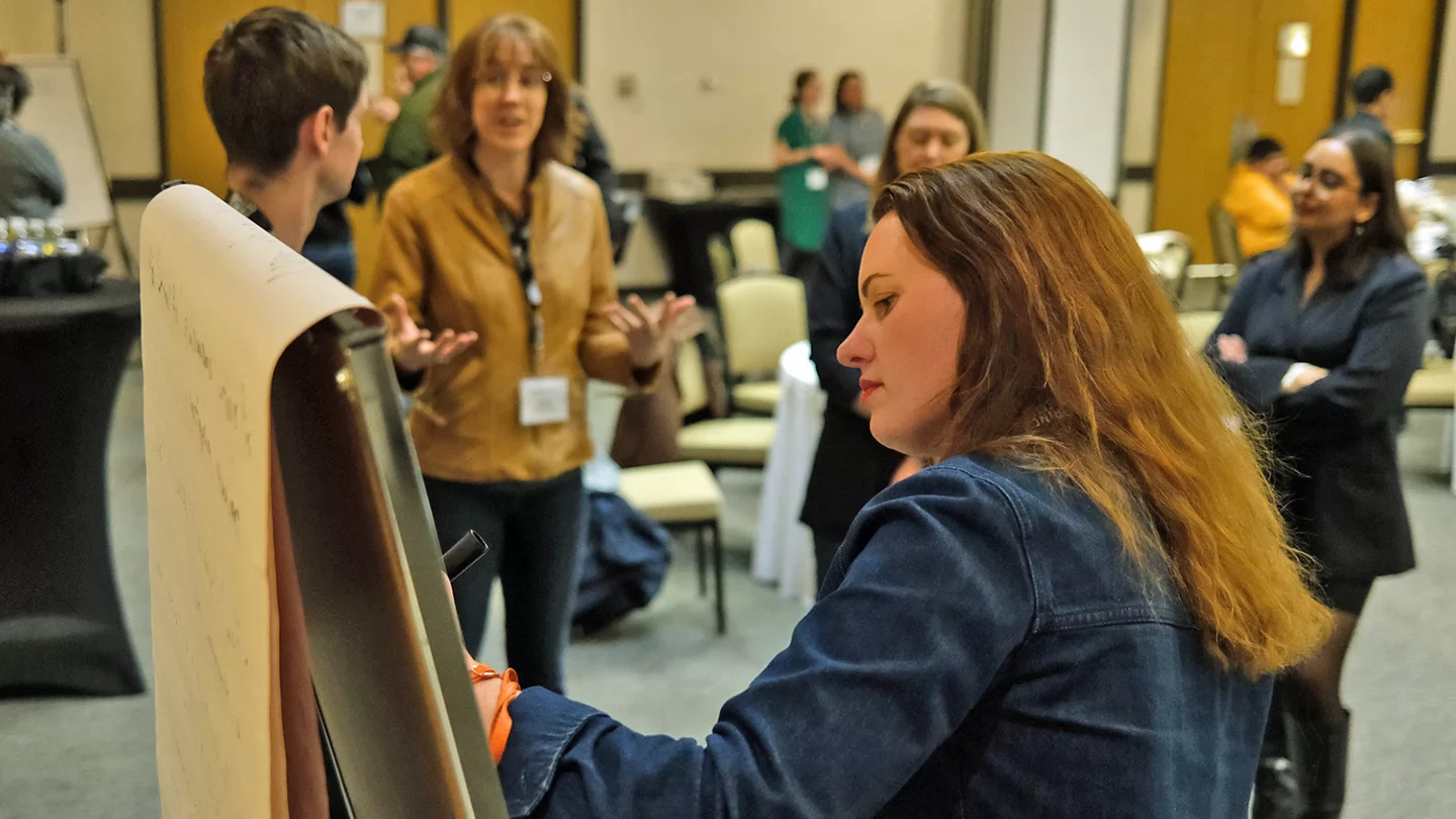Tamara Krawchenko writes on a white board in a busy conference room