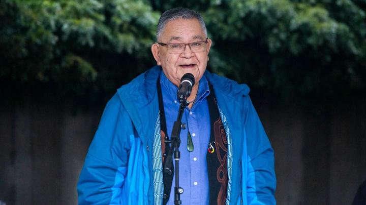 Elder Skip Dick standing in front of a microphone providing a land blessing.