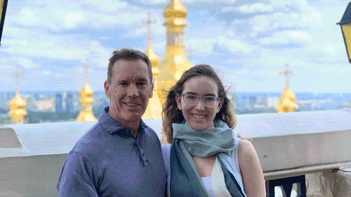 Dale and Sienna stand on a rooftop balcony with city scape behind them