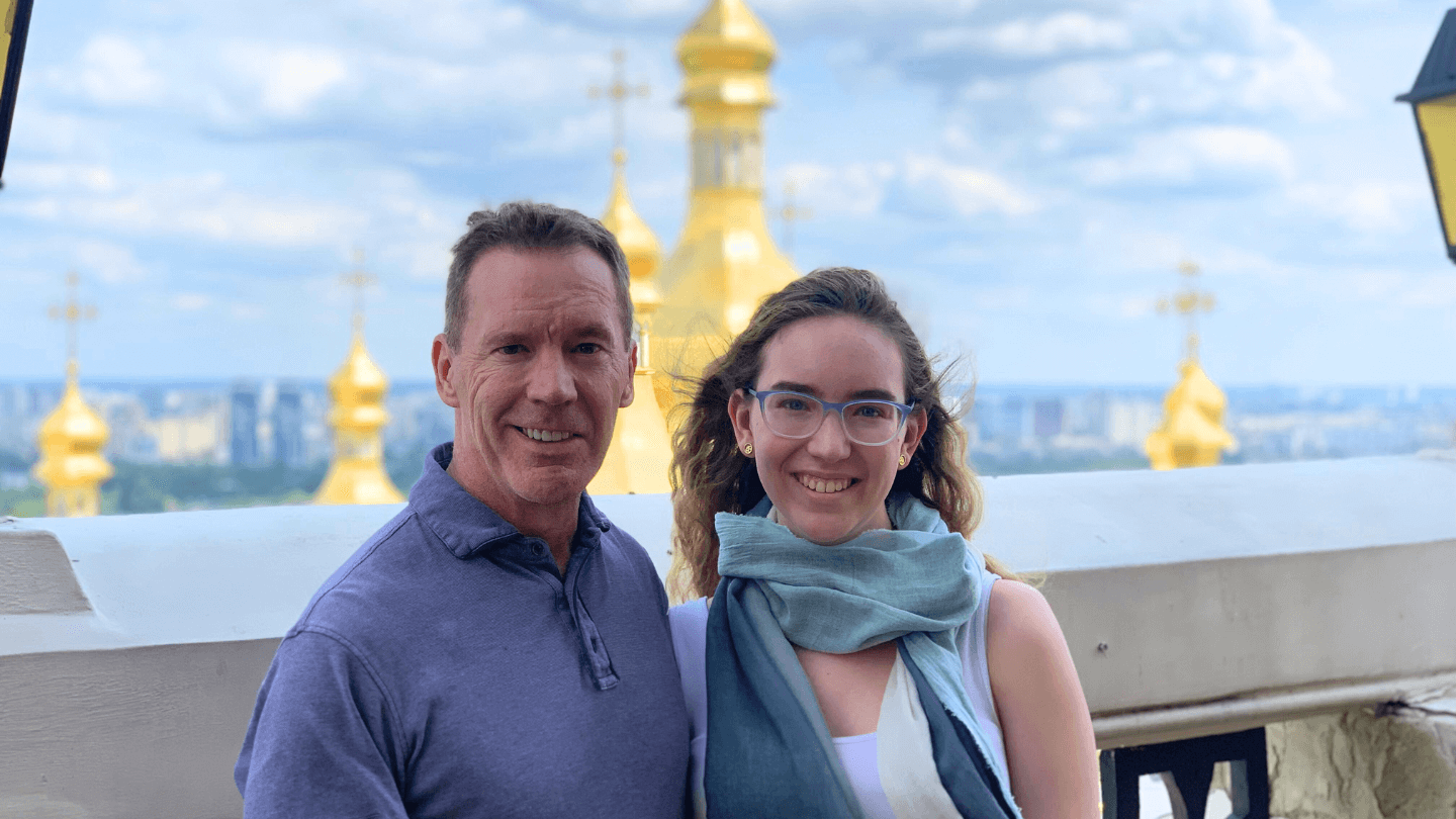 Dale and Sienna stand on a rooftop balcony with city scape behind them 