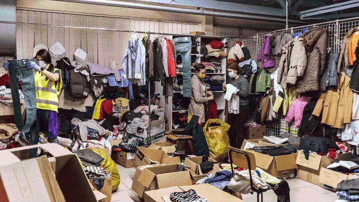 Three people sorting clothes in a room full of clothes on hangers and cardboard boxes