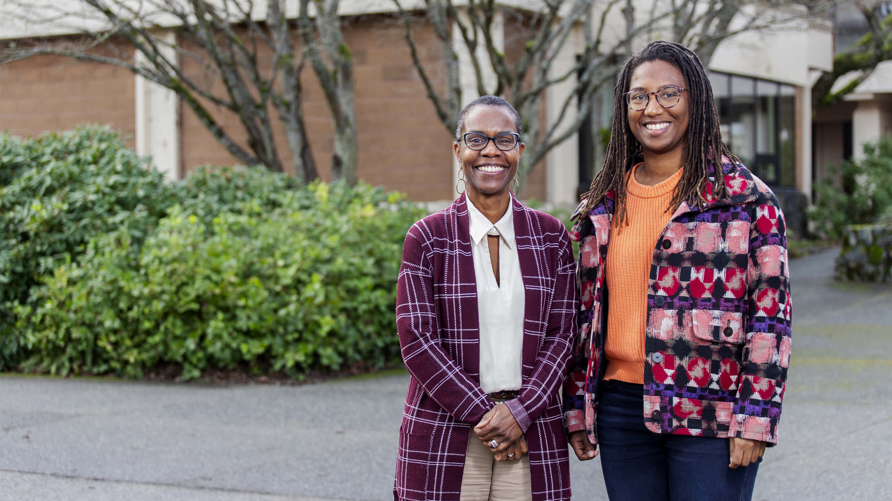Two smiling Black women stand outside on the UVic campus grounds.