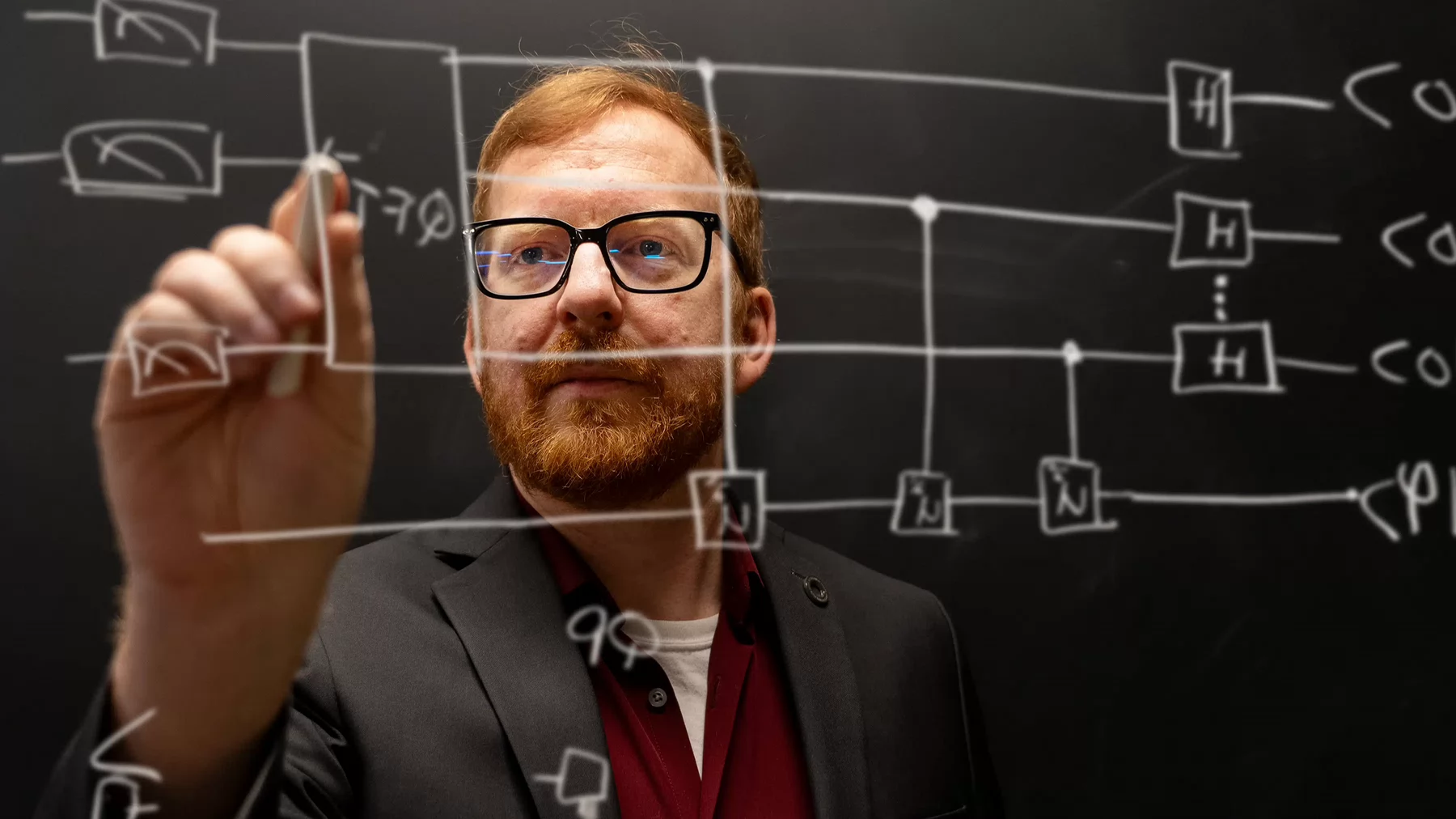 Thomas Baker chalks a quantum diagram on a glass wall.