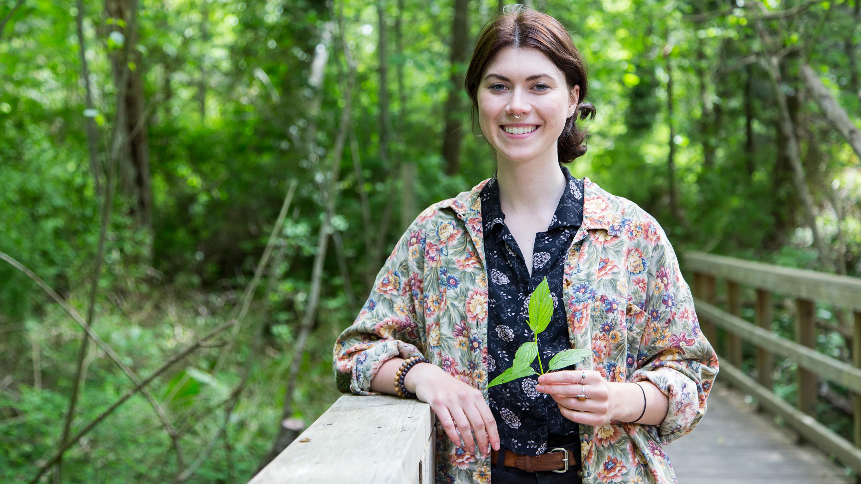 A women poses on a bridge in Bowker creek, holding a branch with leaves.