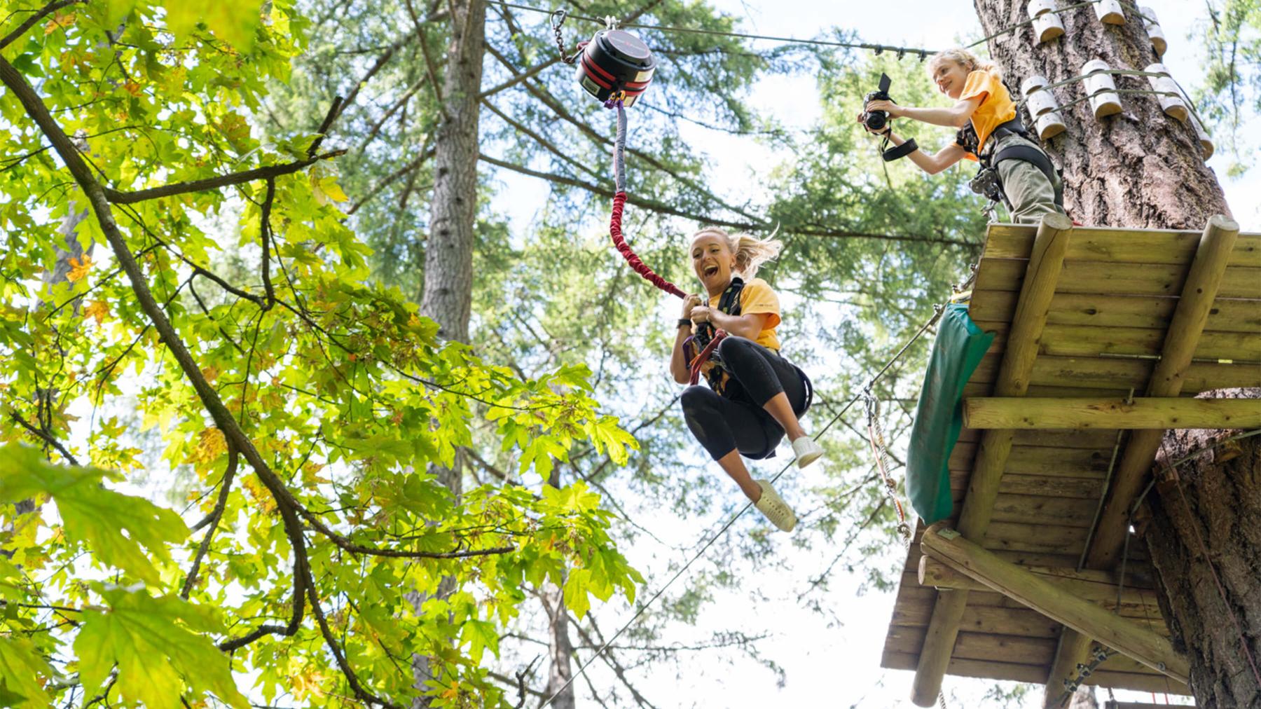 A woman jumps off a platform to ride a zipline through the forest.