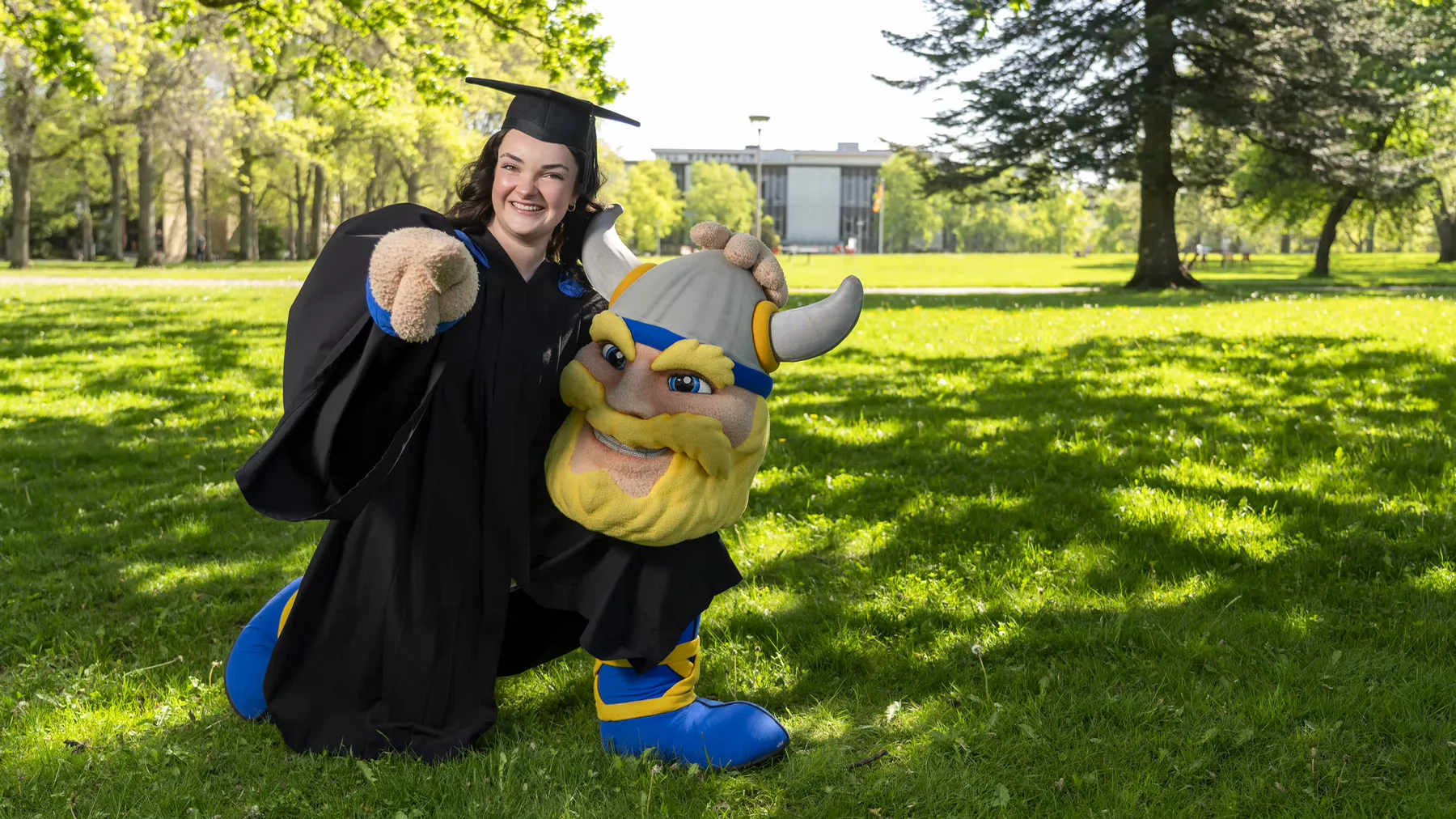 A graduating student dressed in convocation regalia and a mascot outfit..