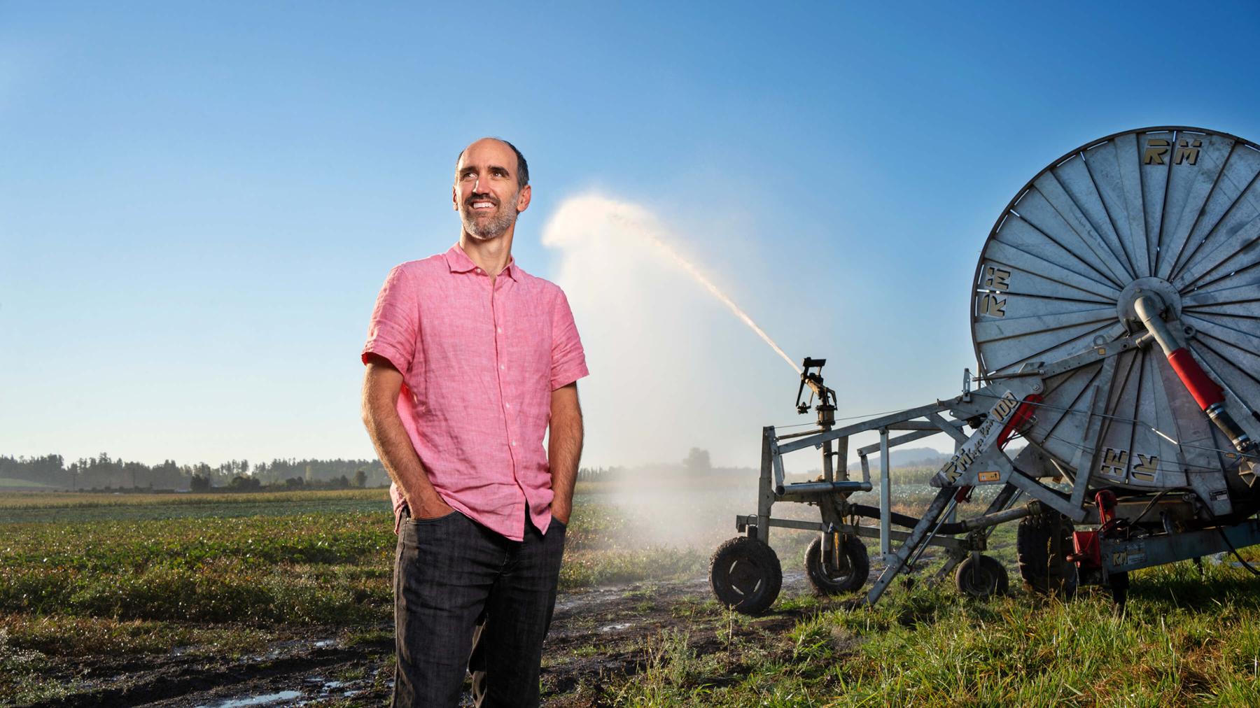 UVic Civil Engineering researcher Tom Gleeson stands in a farm field netx to irrigation equiptment