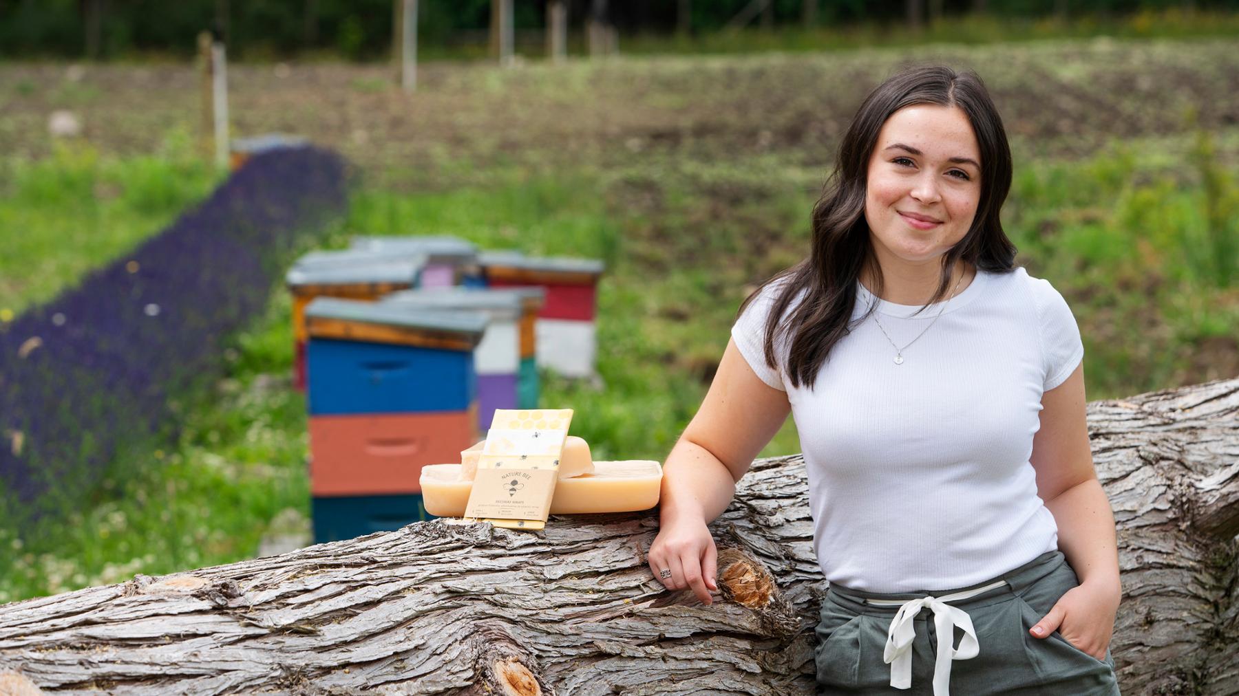 Co-op student Natasha Moroz poses with her eco-friendly beeswax wraps next to some beehives.