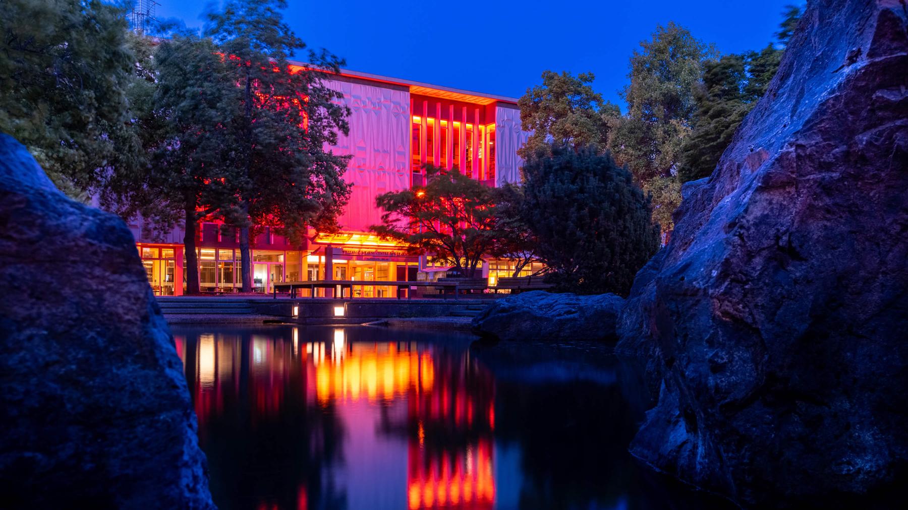 UVic library lit up in orange lights at dusk, in honour of the remains of 215 children found at the former Kamloops Residential School.