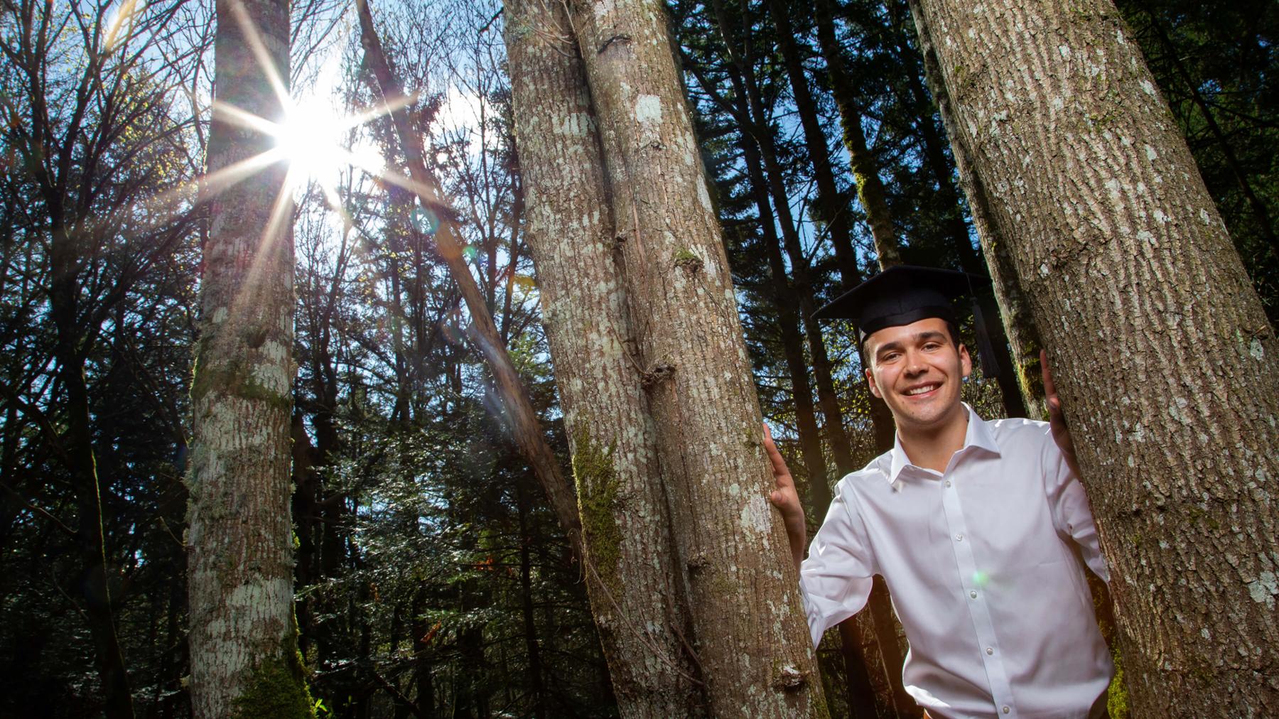 Graduating student Josh poses between trees on UVic campus.