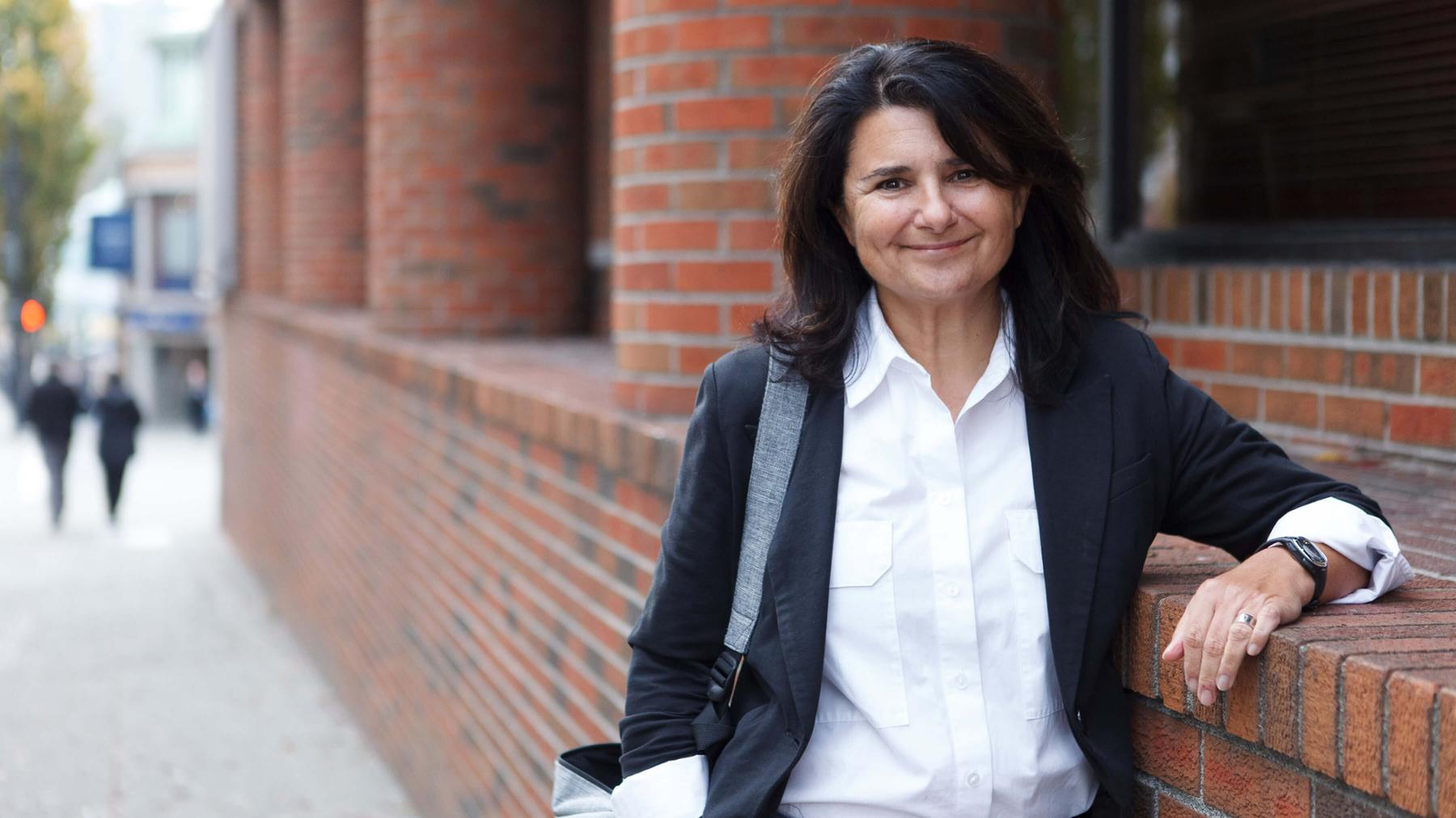 Director of the UVic Social Justice Studies program Nancy Clark leans against a brick wall.
