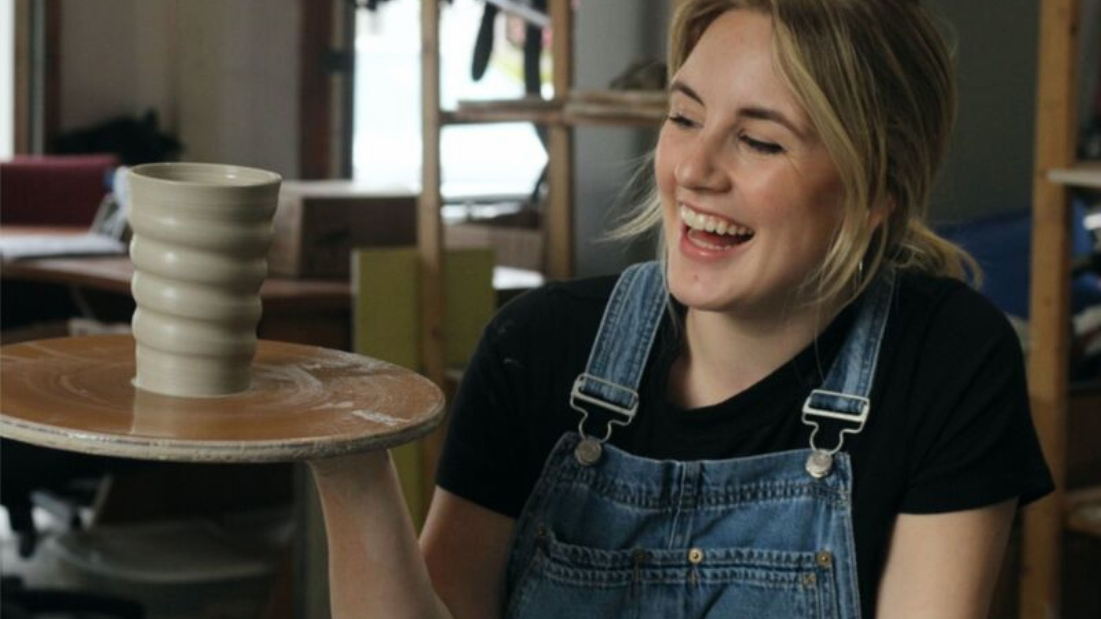 Person smiling looking at a ceramic pot on a pottery wheel