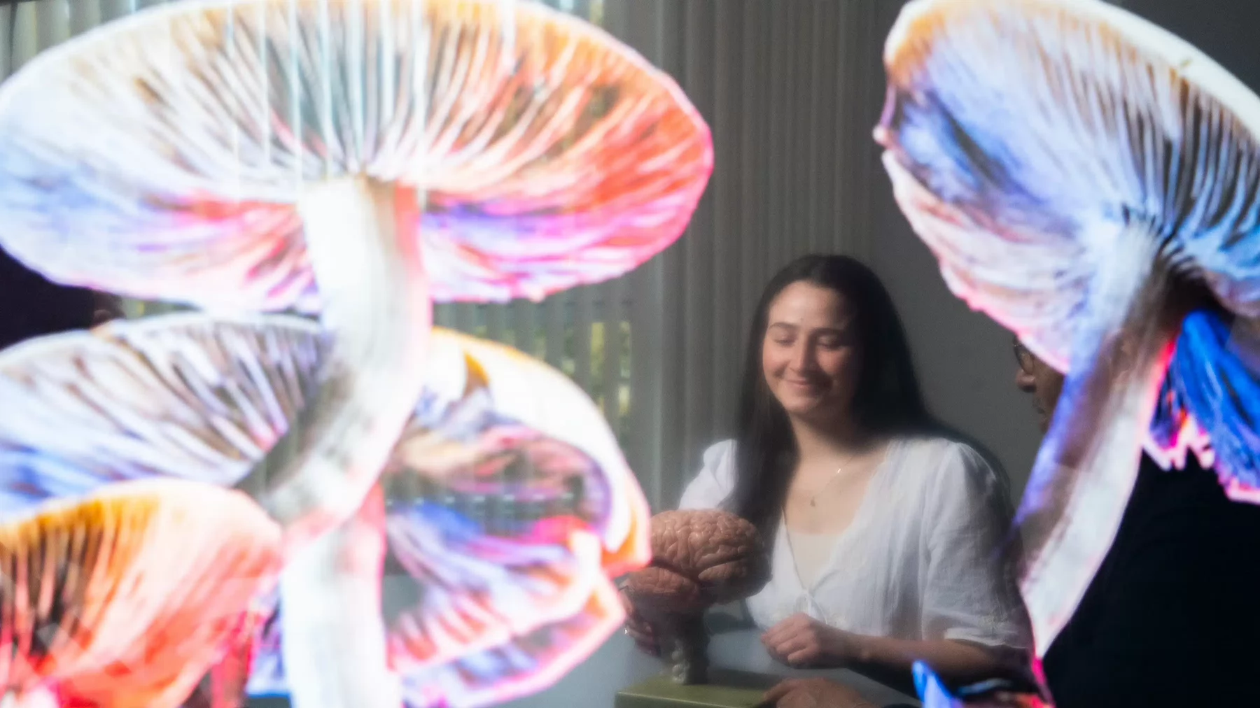 UVic PhD student Baeleigh VanderZwaag sits in a lab surrounded by images of psychedelic mushrooms.
