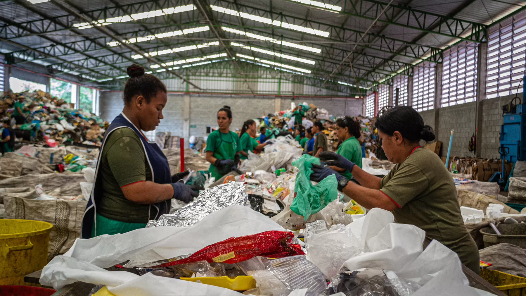 Several people stand along a counter wearing gloves and aprons as they sort through garbage.