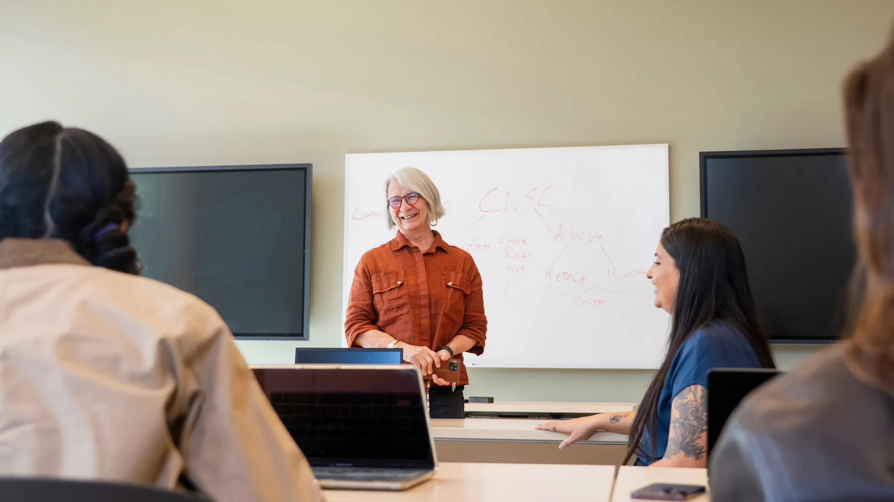 Val Napoleon smiles at the front of a classroom of students.