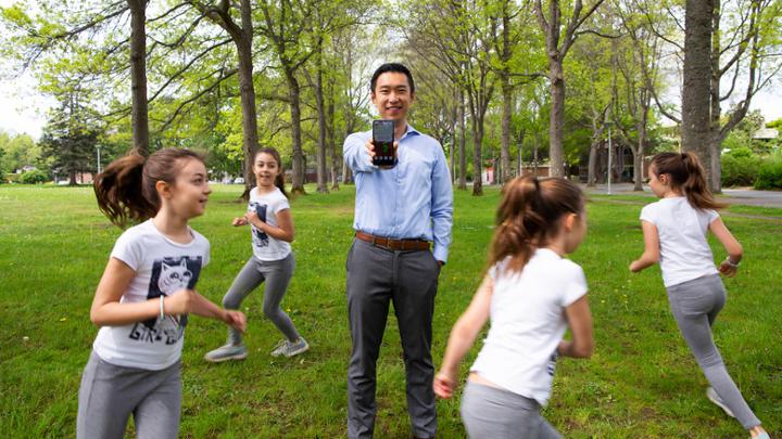 man holding phone with girls running around him