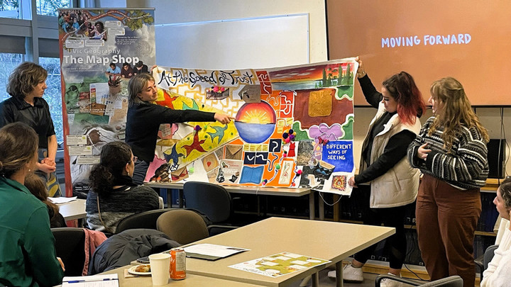 Students stand in front of a colourful poster presentation in a classroom.