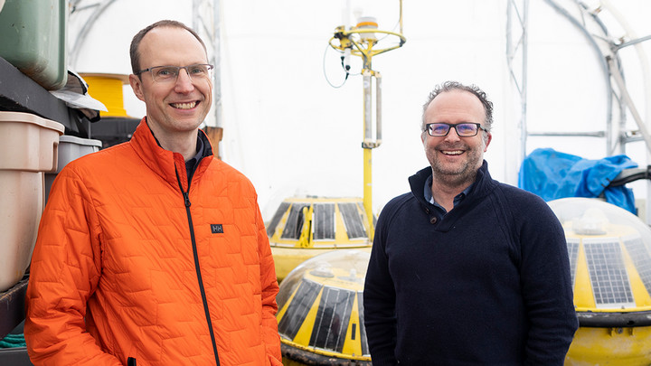 Curran Crawford stands smiling with Brad Buckham with ACET ocean energy survey tech in the background